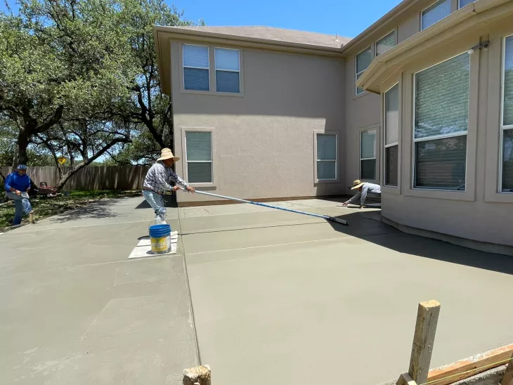 Concrete patio construction in San Antonio, TX with workers pouring cement and smoothing the surface.