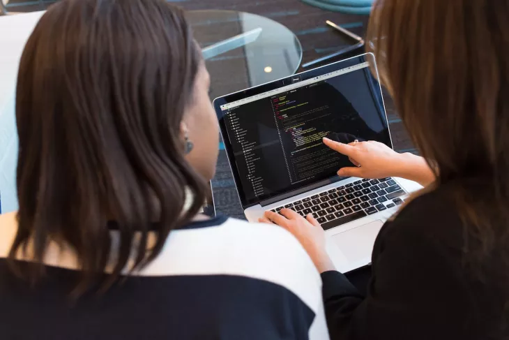 two women looking at code on a computer
