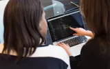 two women looking at code on a computer